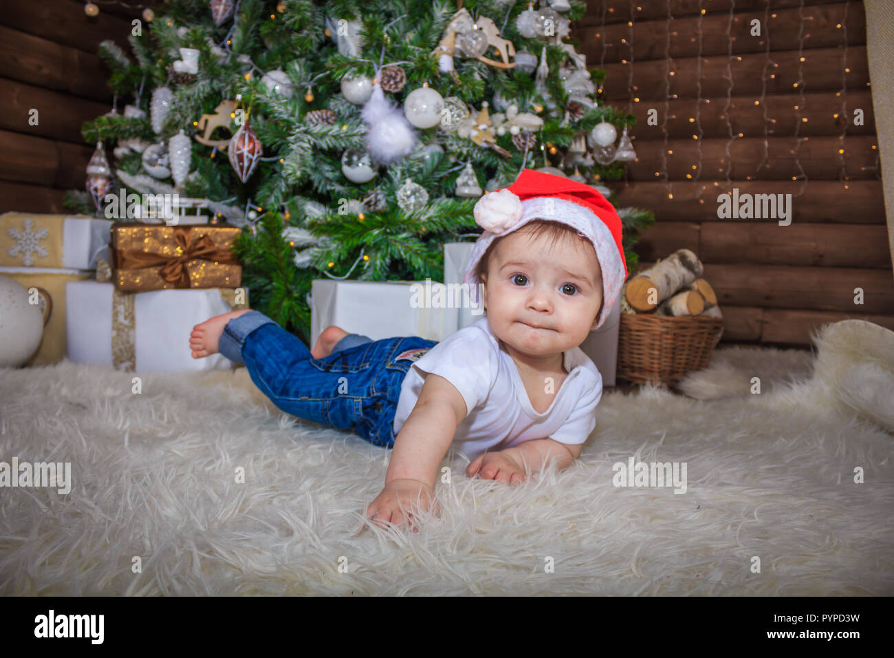 Baby in elf Kostüm spielen mit alten hölzernen Zug und Stofftier Bären unter den Weihnachtsbaum, vintage. Das Baby in die Gap liegt unter dem Baum und sm Stockfoto