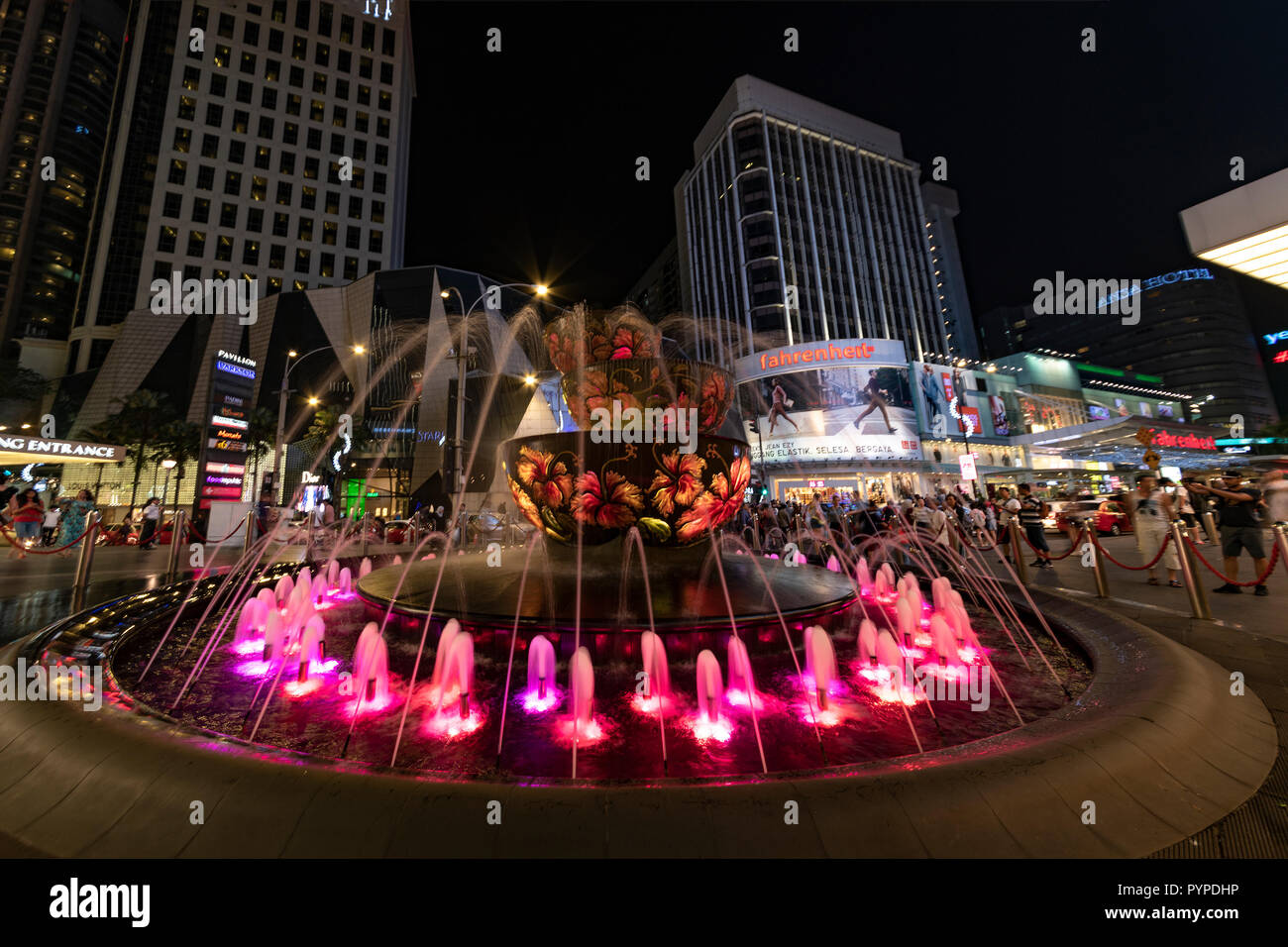 KUALA LUMPUR, 16. August 2018 - Bunte Brunnen vor der beschäftigt und überfüllten 'Pavilion' Einkaufszentrum der Stadt bei Nacht Stockfoto