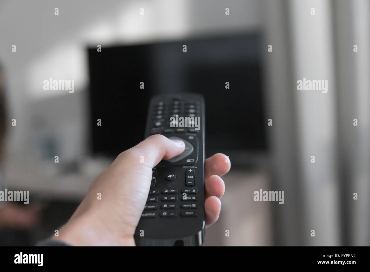 Hand, die Fernbedienung mit Fernsehen Hintergrund in ein Wohnzimmer. Stockfoto