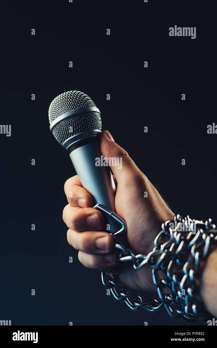 Die Freiheit der Presse und Journalismus, konzeptionelle Bild mit Mikrofon in männlicher Hand mit Ketten, Low Key Image gebunden Stockfoto