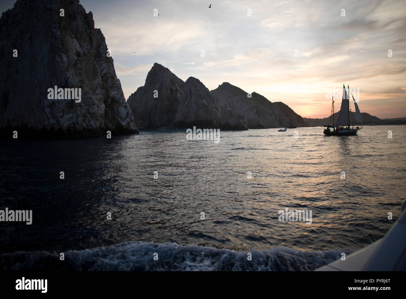 Segelboot Segeln vorbei an großen Felsen im Meer bei Sonnenuntergang. Stockfoto