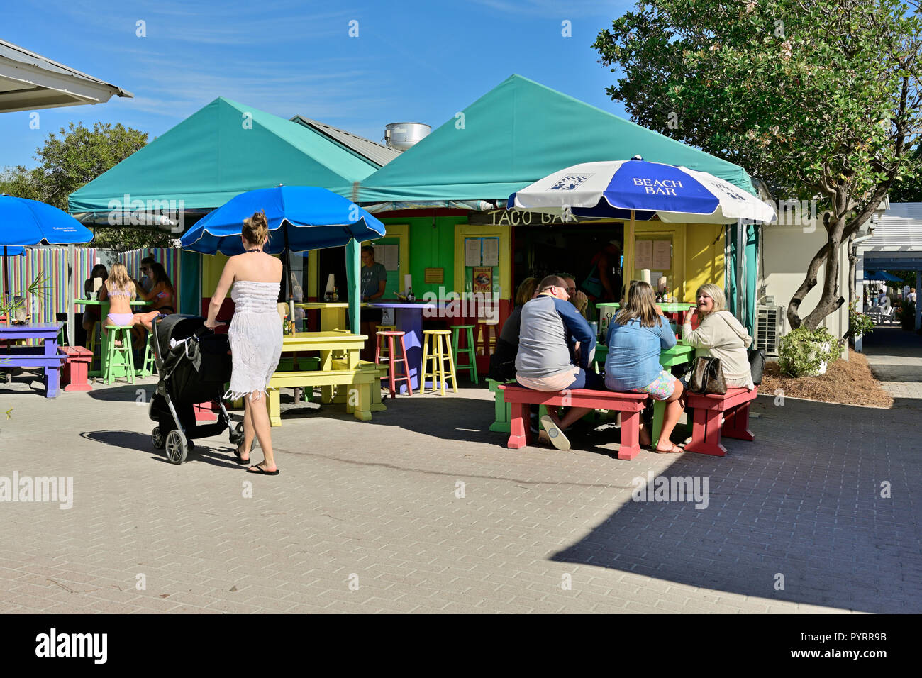 Familie, Mädchen im Teenageralter und eine Mutter mit Kinderwagen zu einem Außenpool Taco Bar Restaurant im Resort Stadt Seaside in Florida, USA. Stockfoto