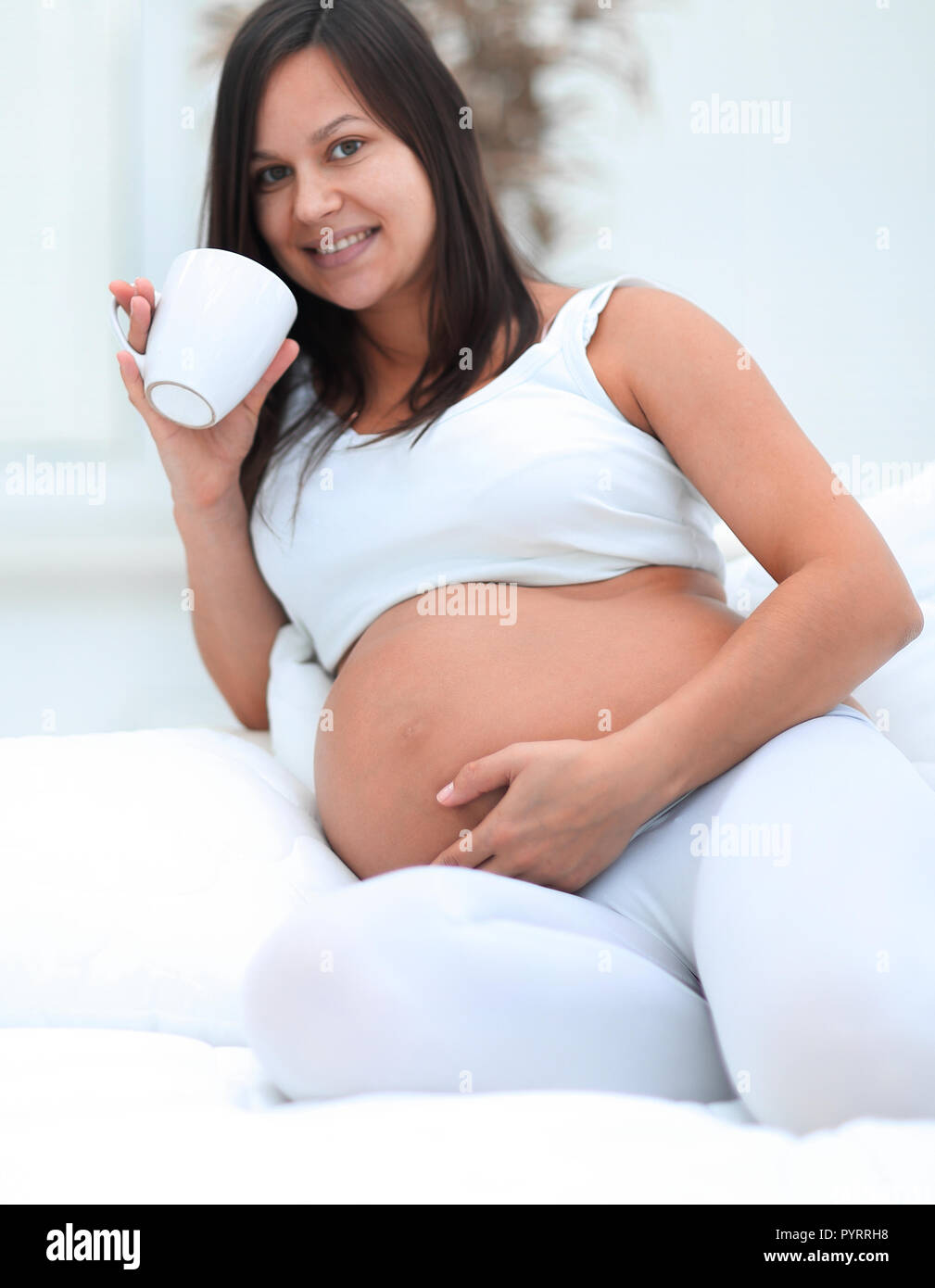 Glücklich schwanger Frau trinkt Milch im Wohnzimmer sitzen. Stockfoto