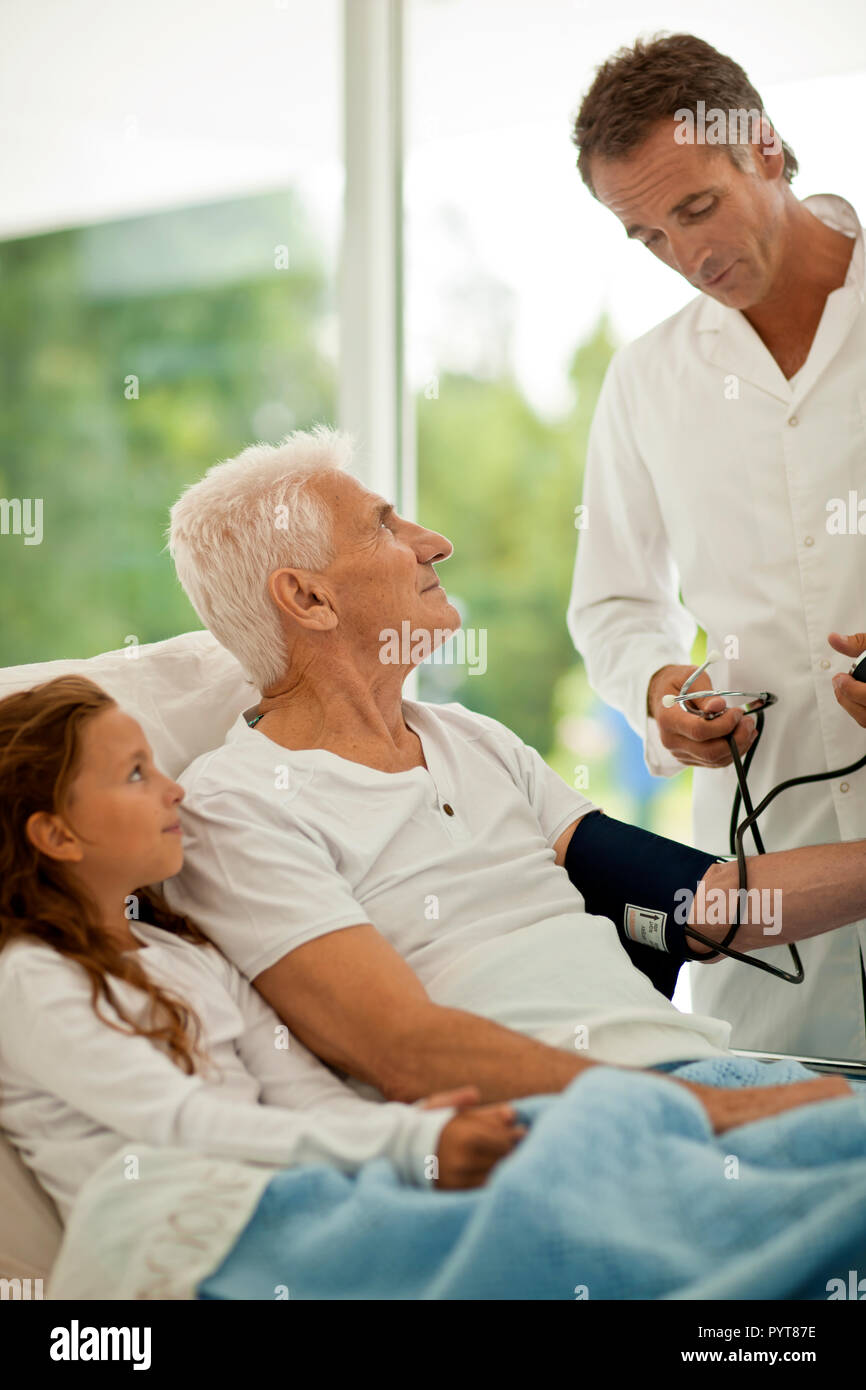 Der Mensch seinen Blutdruck in ein Krankenhaus gebracht, während ein Besuch von seiner Enkelin. Stockfoto