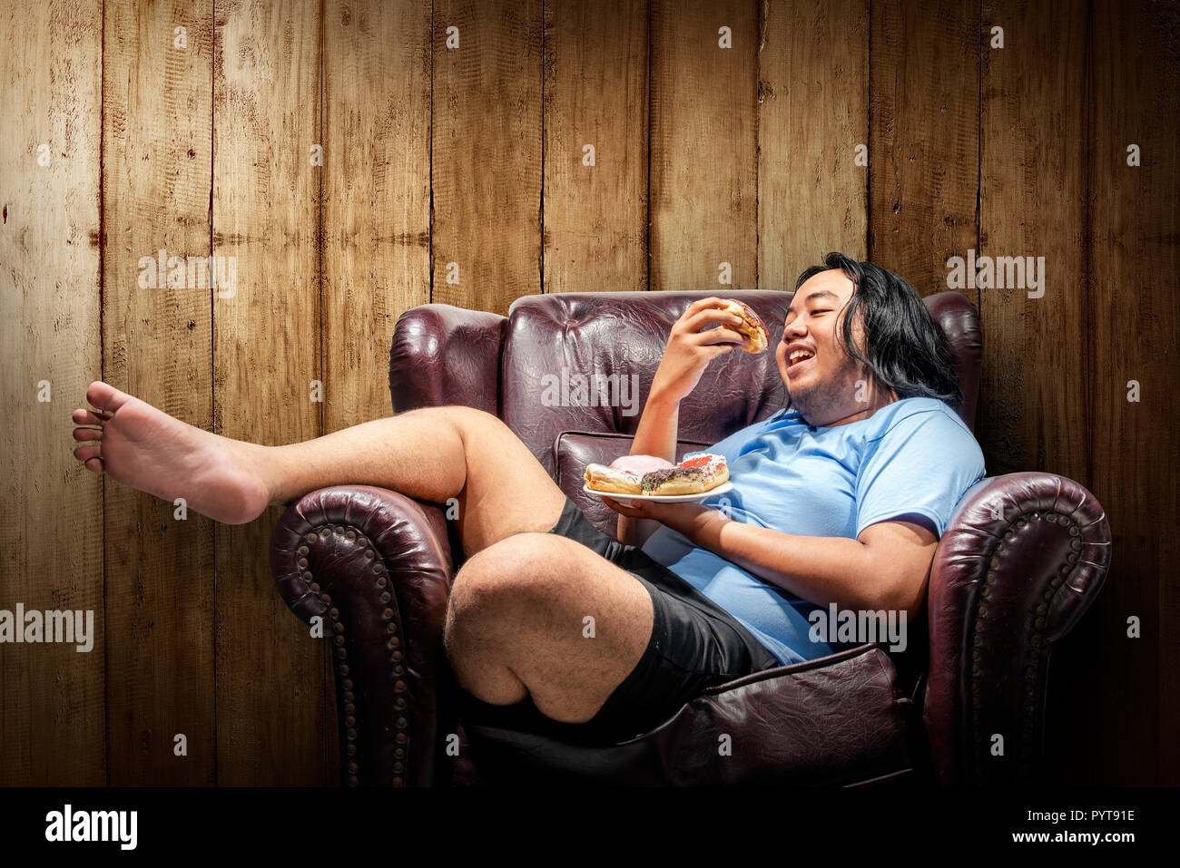 Asiatische Fat Man donuts Essen auf dem Teller auf dem Sofa. Fat Man Diät Konzept Stockfoto
