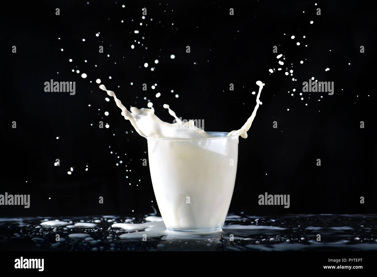 Spritzer Milch aus einem Glas transparent Glas, fliegen in alle Richtungen, auf die in der Tabelle auf einem schwarzen Hintergrund. Stockfoto