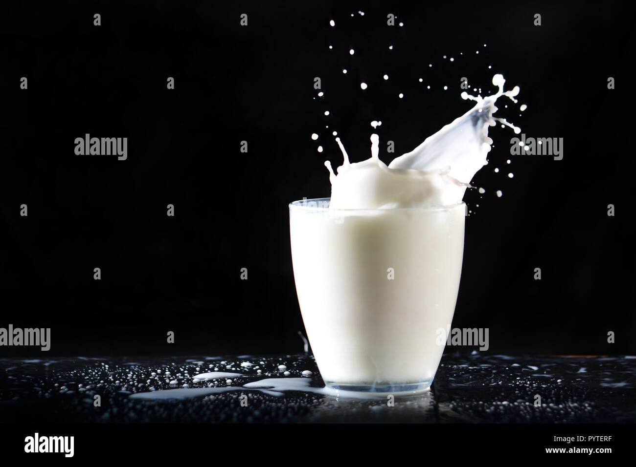 Reichlich Milch spritzt aus Glas Glas, fliegen in alle Richtungen, auf die in der Tabelle auf einem schwarzen Hintergrund. Stockfoto