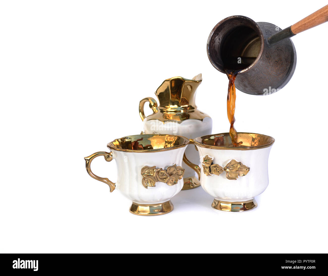 Kaffee fließt in eine weiße Tasse mit einem goldenen Griff und eine Blume. Zwei Tassen und ein Milchkännchen. Stockfoto