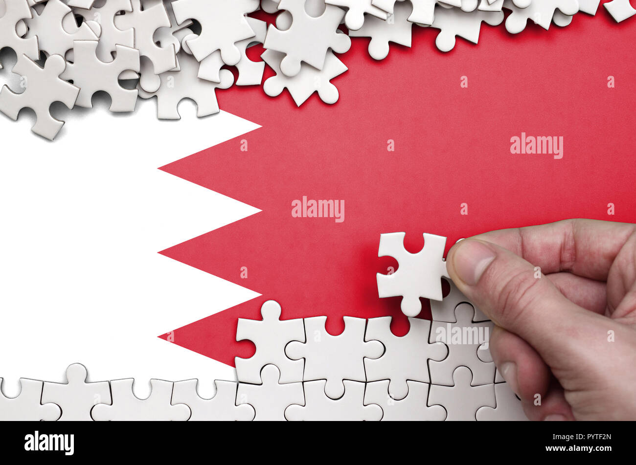 Bahrain Fahne wird auf einen Tisch, auf dem die menschliche Hand ein Puzzle von weißer Farbe Falten dargestellt. Stockfoto