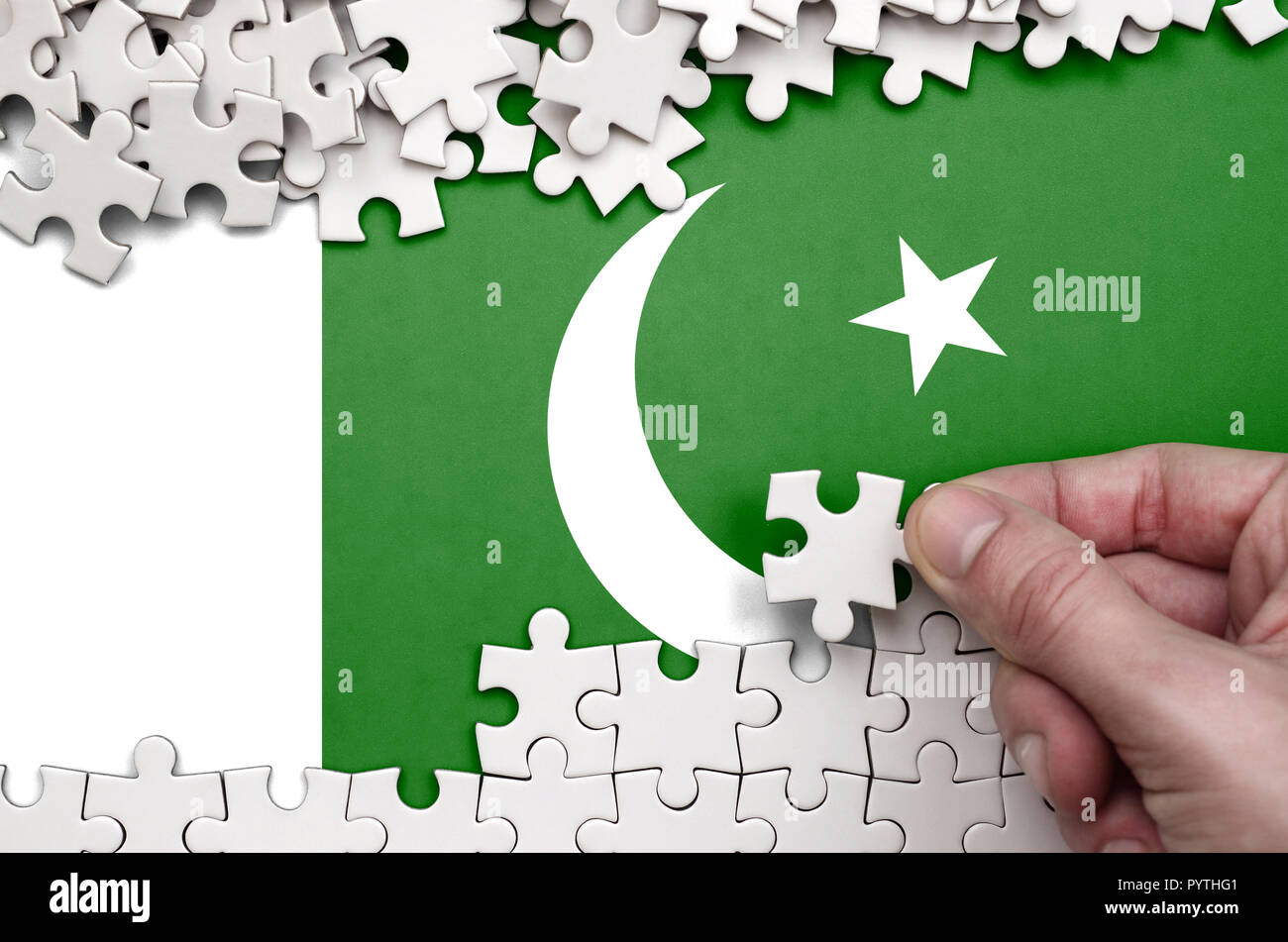 Pakistan Fahne wird auf einen Tisch, auf dem die menschliche Hand ein Puzzle von weißer Farbe Falten dargestellt. Stockfoto