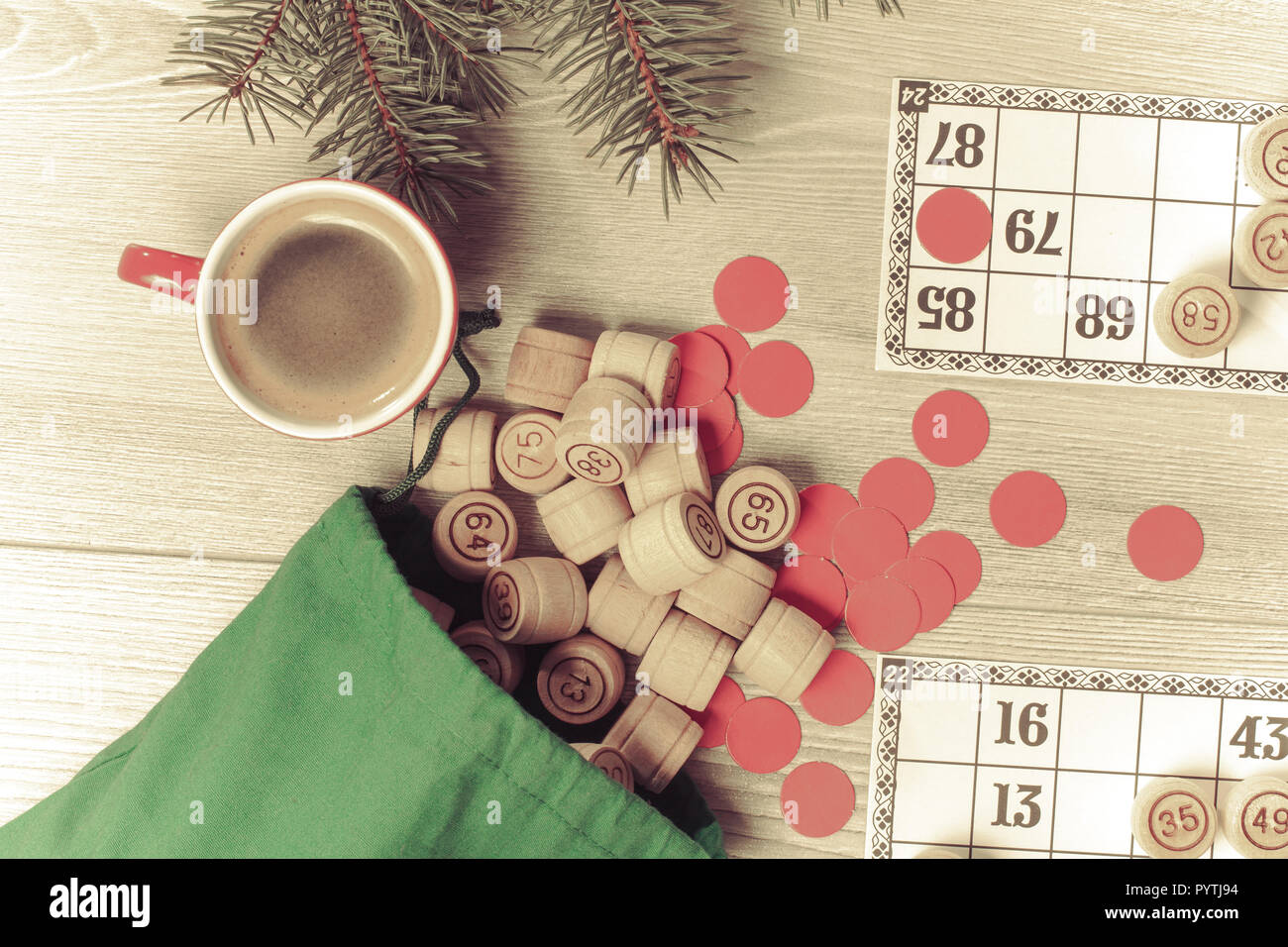 Board Game Lotto. Holz- lotto Fässer mit grün Beutel, Spielkarten, rote Chips und Tasse Kaffee, Weihnachten Tannenbaum Äste. Ansicht von oben. Farbe toning ef Stockfoto