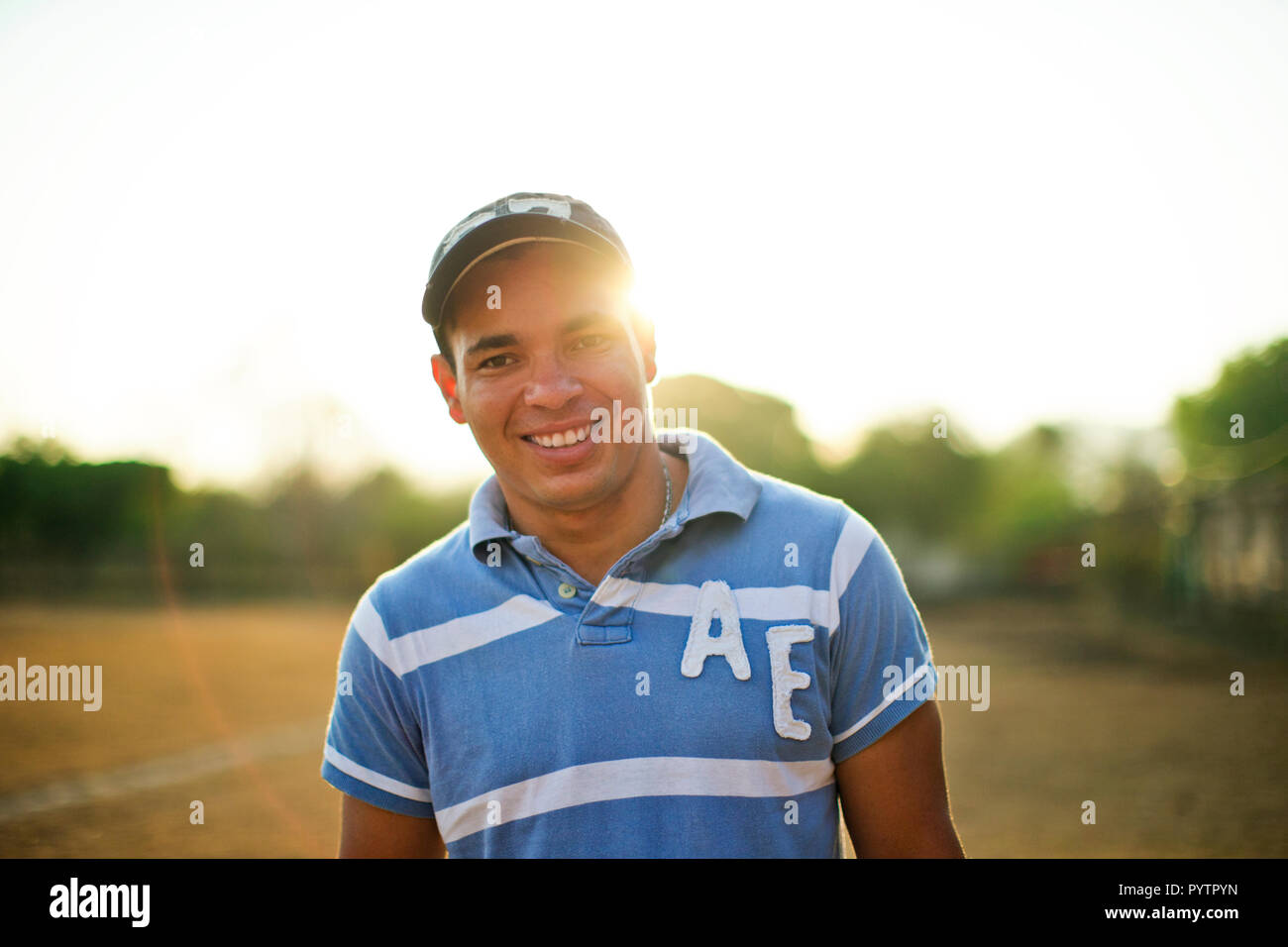 Porträt eines lächelnden jungen Mann, der auf einem grasbewachsenen Sportplatz in der Sonne. Stockfoto