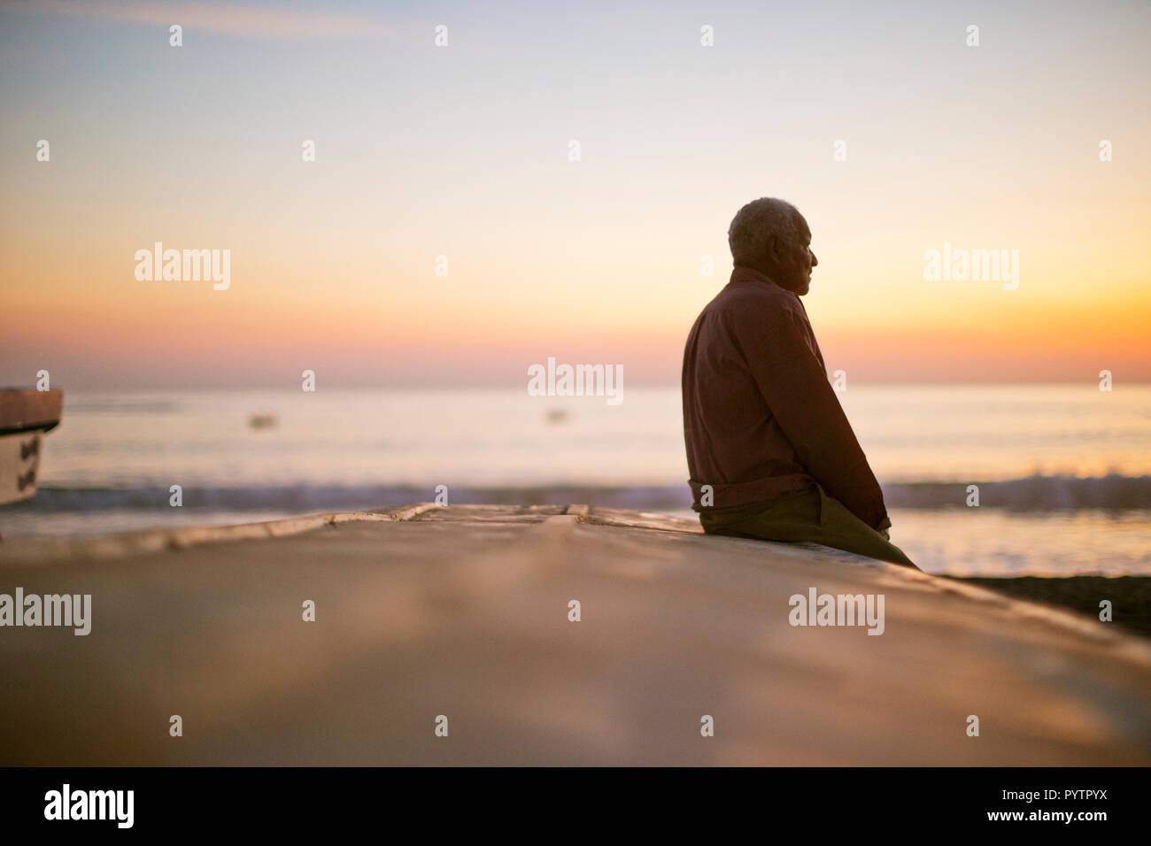 Nachdenklich reifer Mann sitzt auf einem Strand bei Sonnenuntergang. Stockfoto