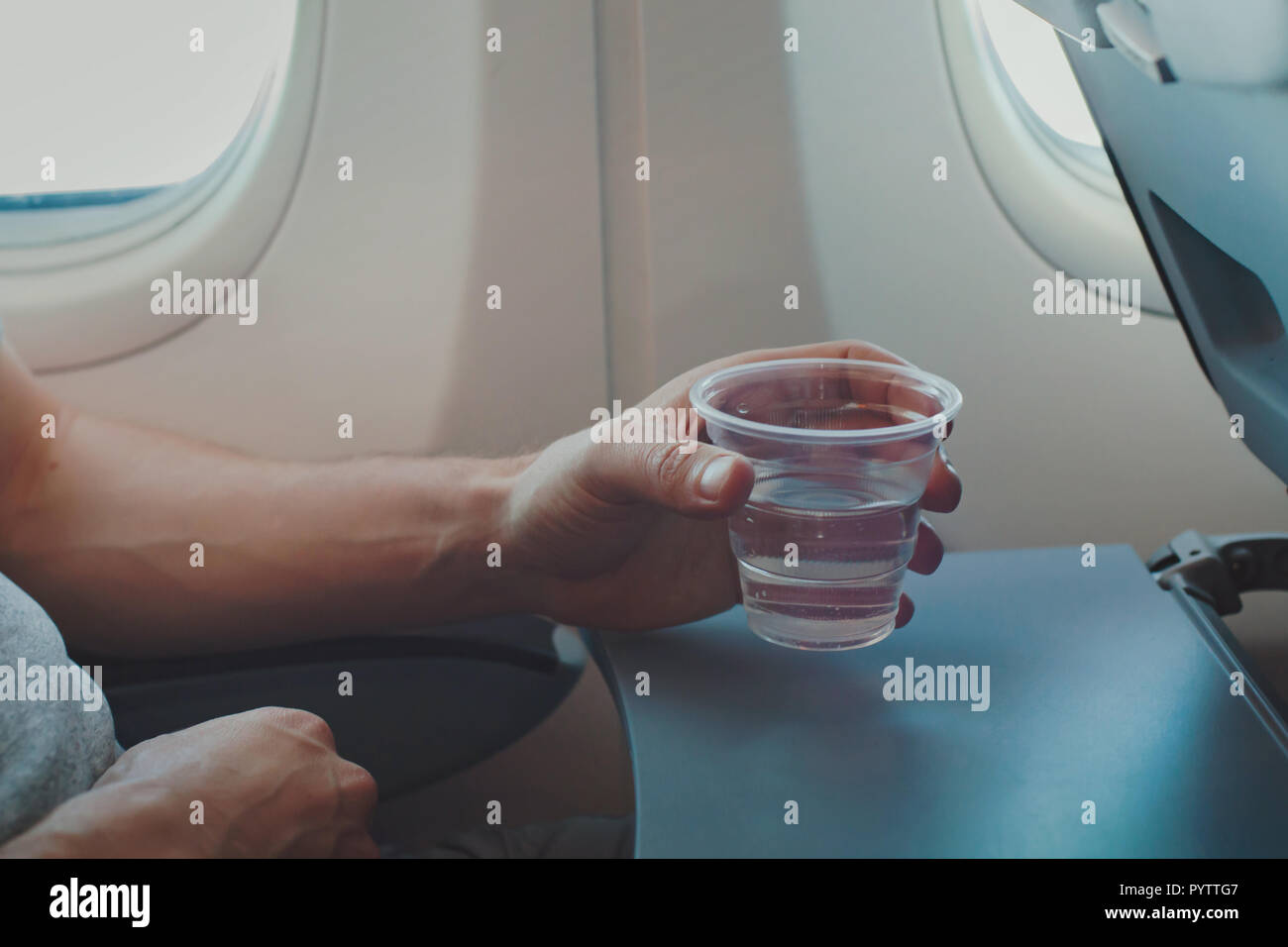 Passagier Trinkwasser im Flugzeug während des Fluges. Nahaufnahme einer Hand, die Glas in der Ebene. Stockfoto