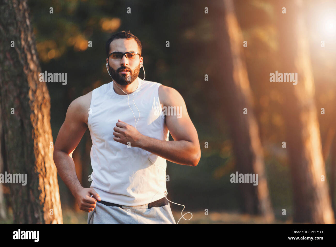 Multikulturelle aussehenden bärtigen Mann in Sportkleidung seine Lieblingsmusik hören und mit seinen Morgen im Wald laufen, gesunden Lebensstil und Personen Konzept Stockfoto