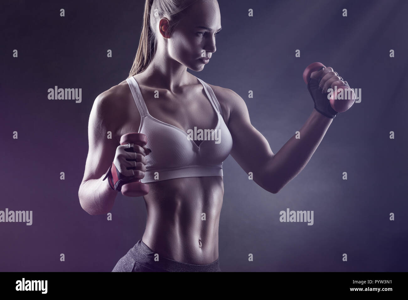 Junge athletische Frau mit Hanteln vor einem dunklen Hintergrund Stockfoto