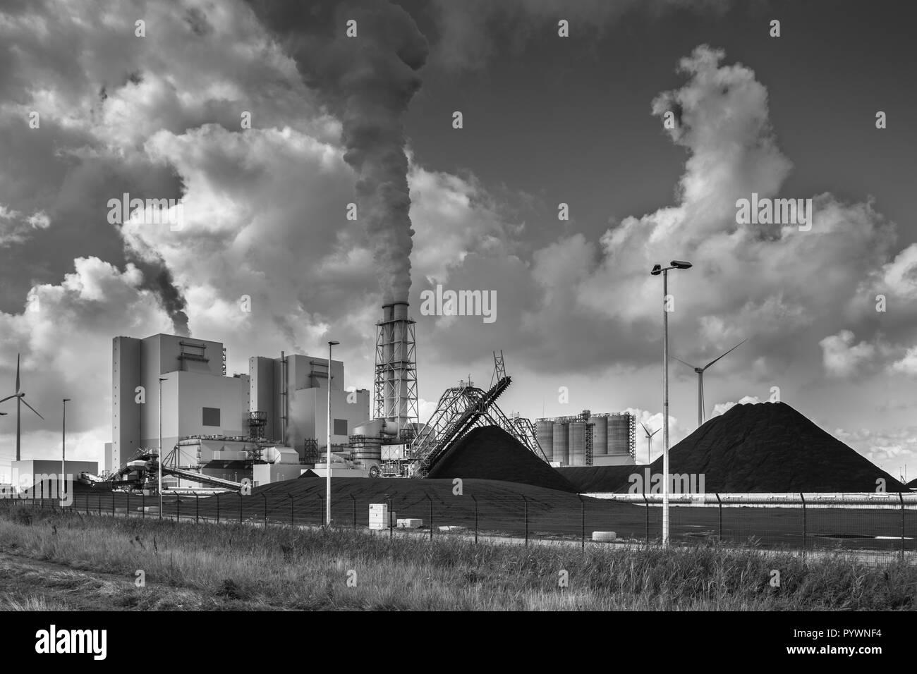 Schwere industrielle Anlage mit Rohren und Rauch und Unmengen von Kohle in Schwarz und Weiß Stockfoto