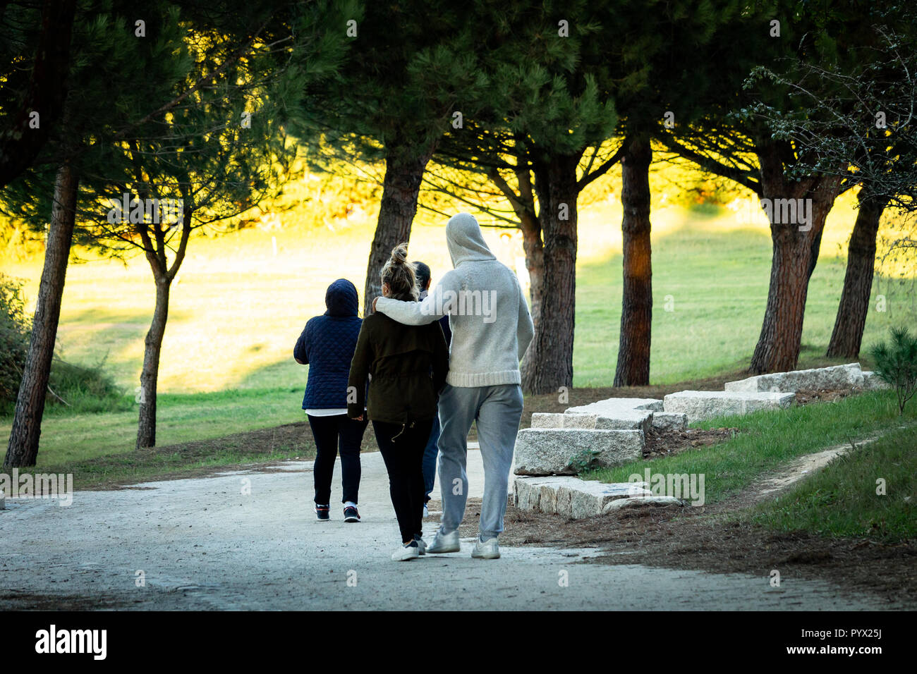 Ein junges Paar Spaziergänge im Park mit warmem Licht im Hintergrund. Blick nach hinten, Hoodie. Stockfoto