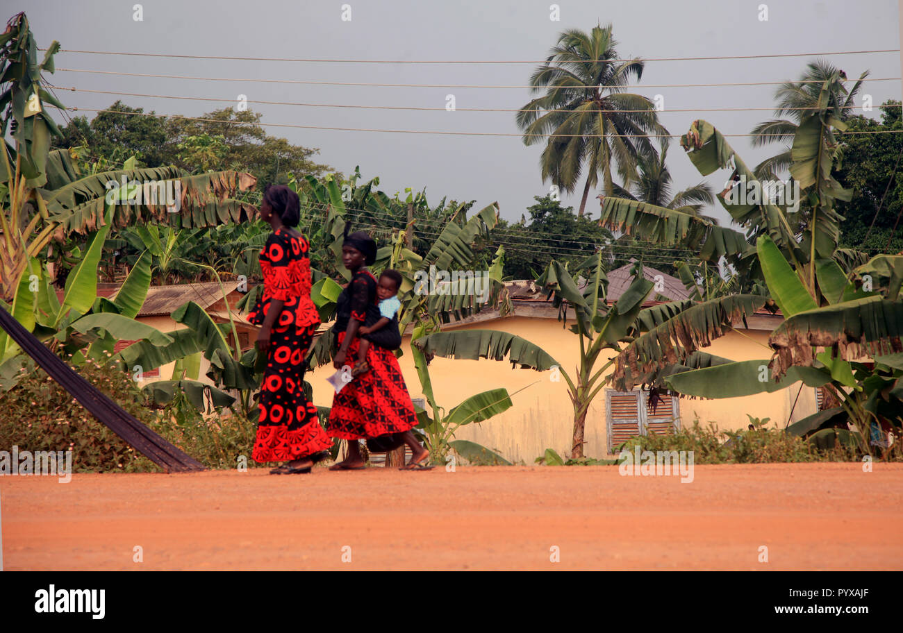 Zwei Frauen und ein Baby Spaziergang entlang einem Feldweg in rot gekleidet und Schwarz für die Beerdigung, die Sie gerade besucht, Odumase Abrafo, Ghana Stockfoto