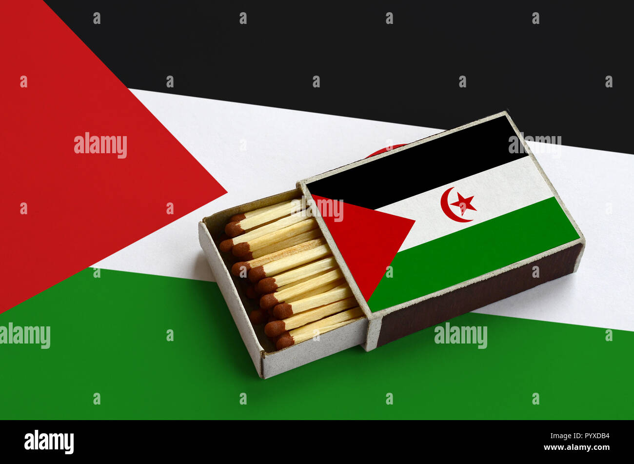 Westsahara Flagge ist in einer offenen Streichholzschachtel, die mit Streichhölzern gefüllt ist und liegt auf einer großen Flagge gezeigt. Stockfoto