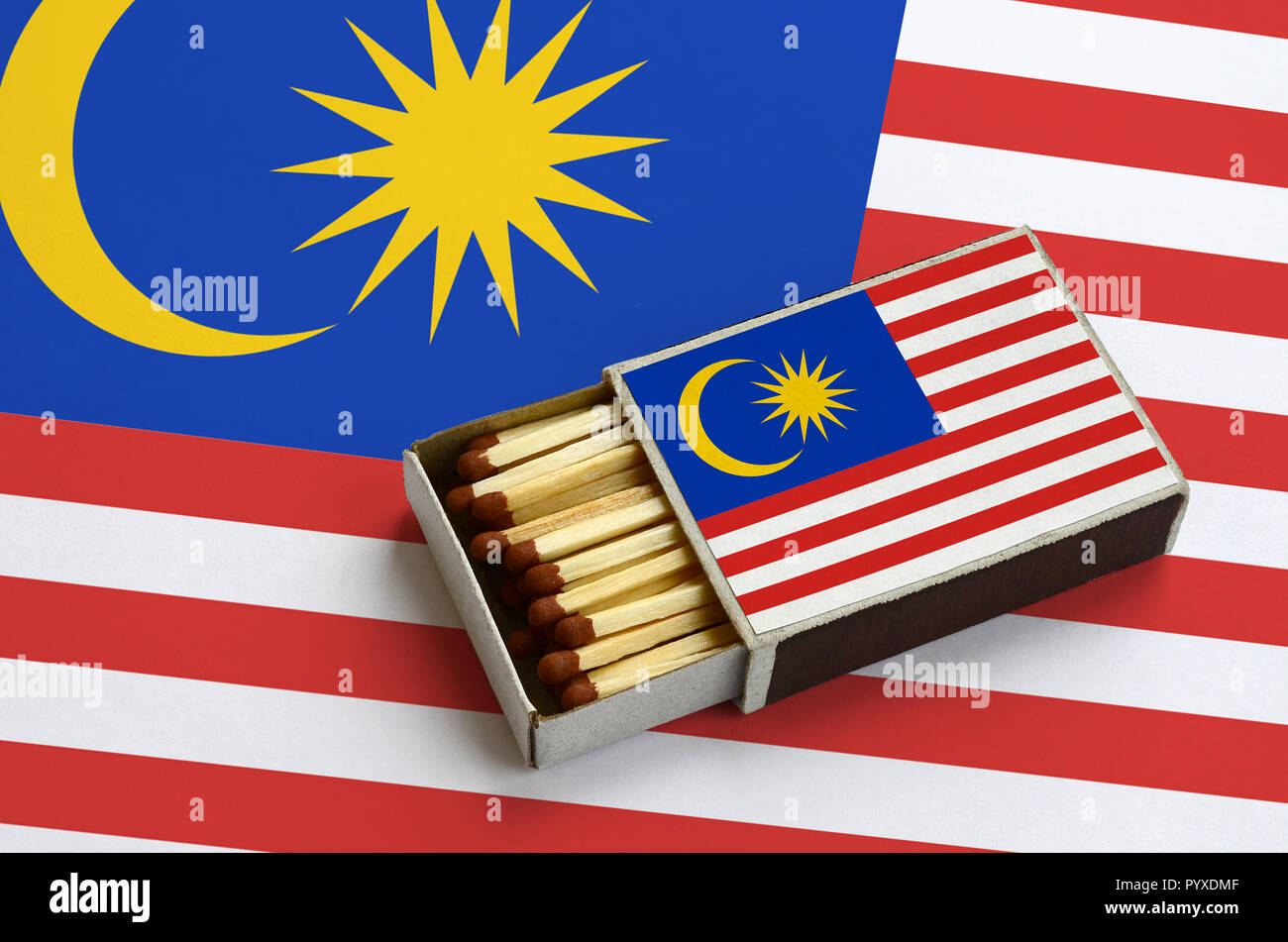 Malaysia Fahne ist in einer offenen Streichholzschachtel, die mit Streichhölzern gefüllt ist und liegt auf einer großen Flagge gezeigt. Stockfoto