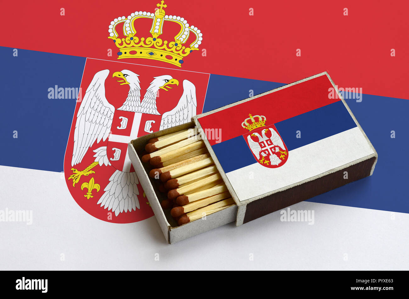Serbien Flagge ist in einer offenen Streichholzschachtel, die mit Streichhölzern gefüllt ist und liegt auf einer großen Flagge gezeigt. Stockfoto