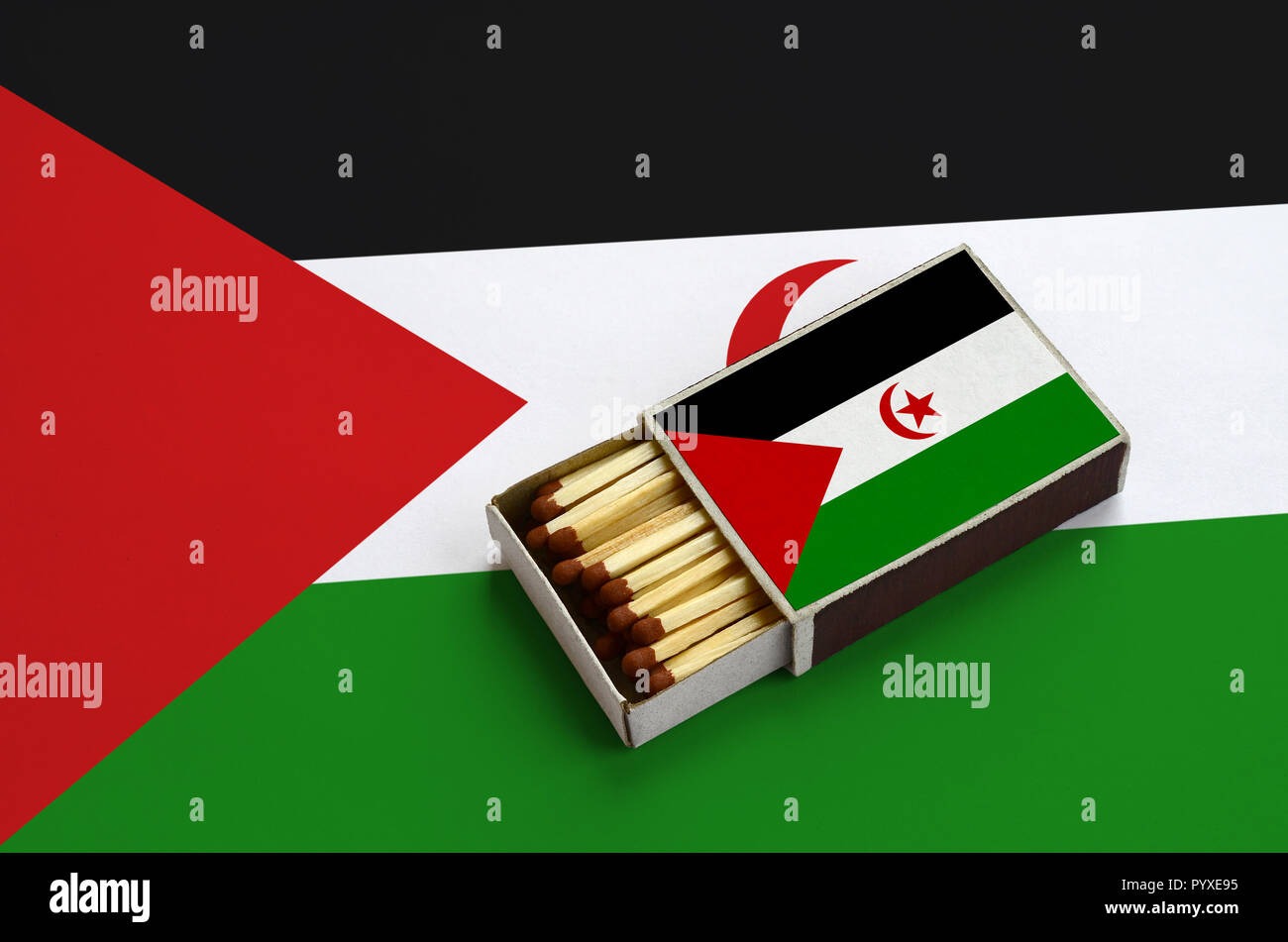 Westsahara Flagge ist in einer offenen Streichholzschachtel, die mit Streichhölzern gefüllt ist und liegt auf einer großen Flagge gezeigt. Stockfoto