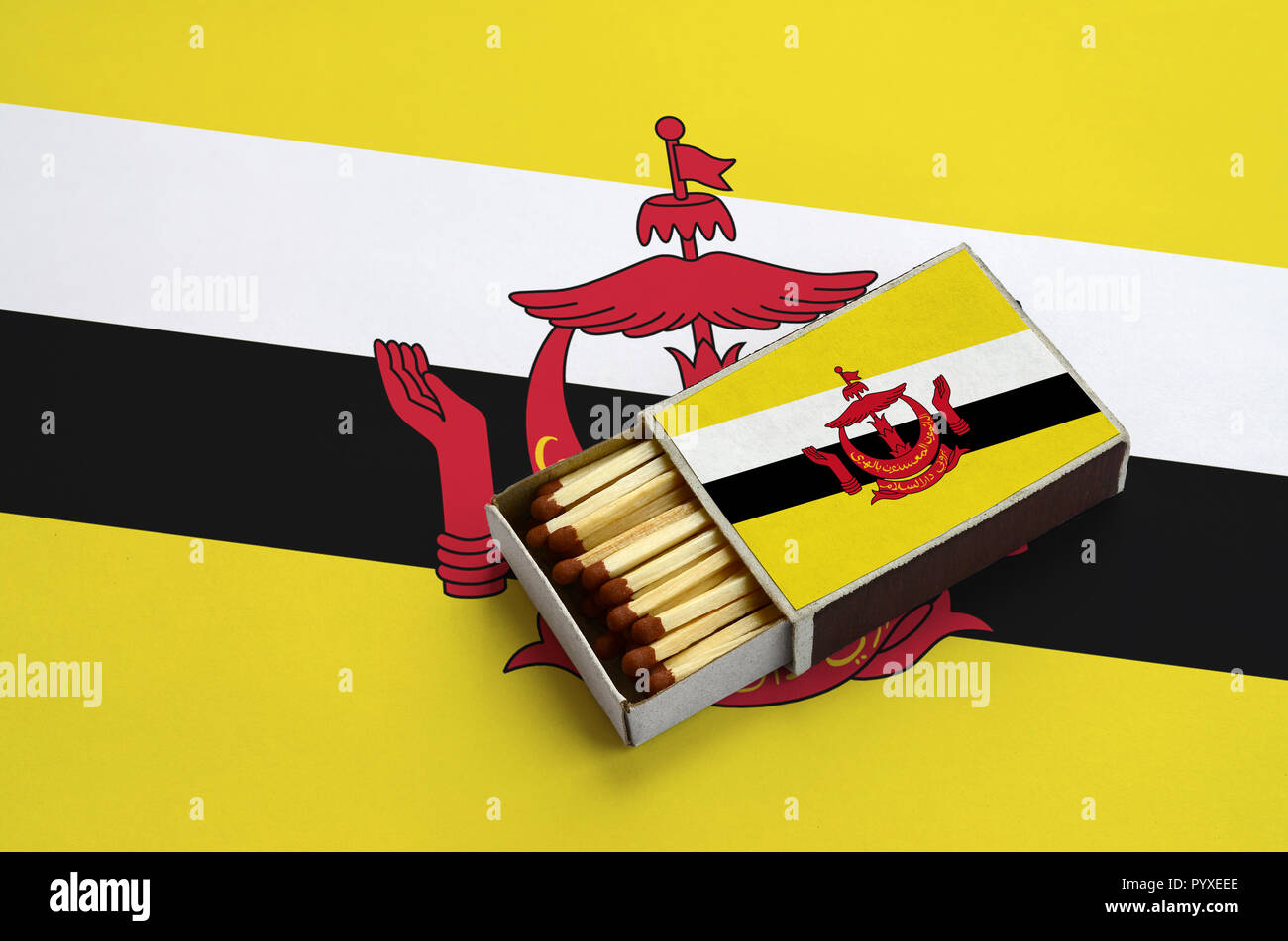 Brunei Darussalam Flagge ist in einer offenen Streichholzschachtel, die mit Streichhölzern gefüllt ist und liegt auf einer großen Flagge gezeigt. Stockfoto