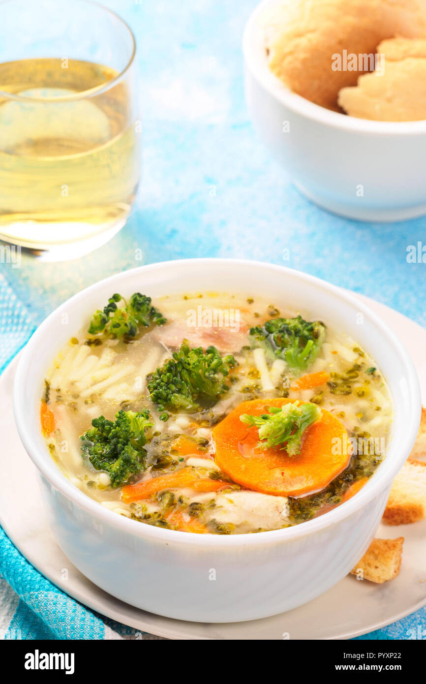 Italienische Gemüsesuppe mit Brokkoli Möhren Nudeln in Hühnerbrühe auf blauen Tisch mit Scheiben Brot und Glas Saft. Essen vegetarische organischen Stil Stockfoto