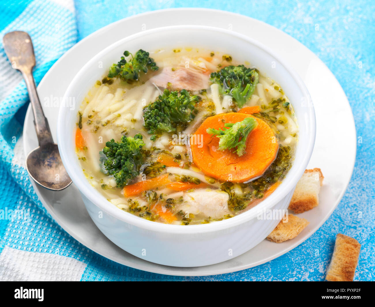 Italienische Gemüsesuppe mit Brokkoli Möhren Nudeln in Hühnerbrühe auf blauen Tisch mit Scheiben Brot und Glas Saft. Essen vegetarische organischen Stil Stockfoto