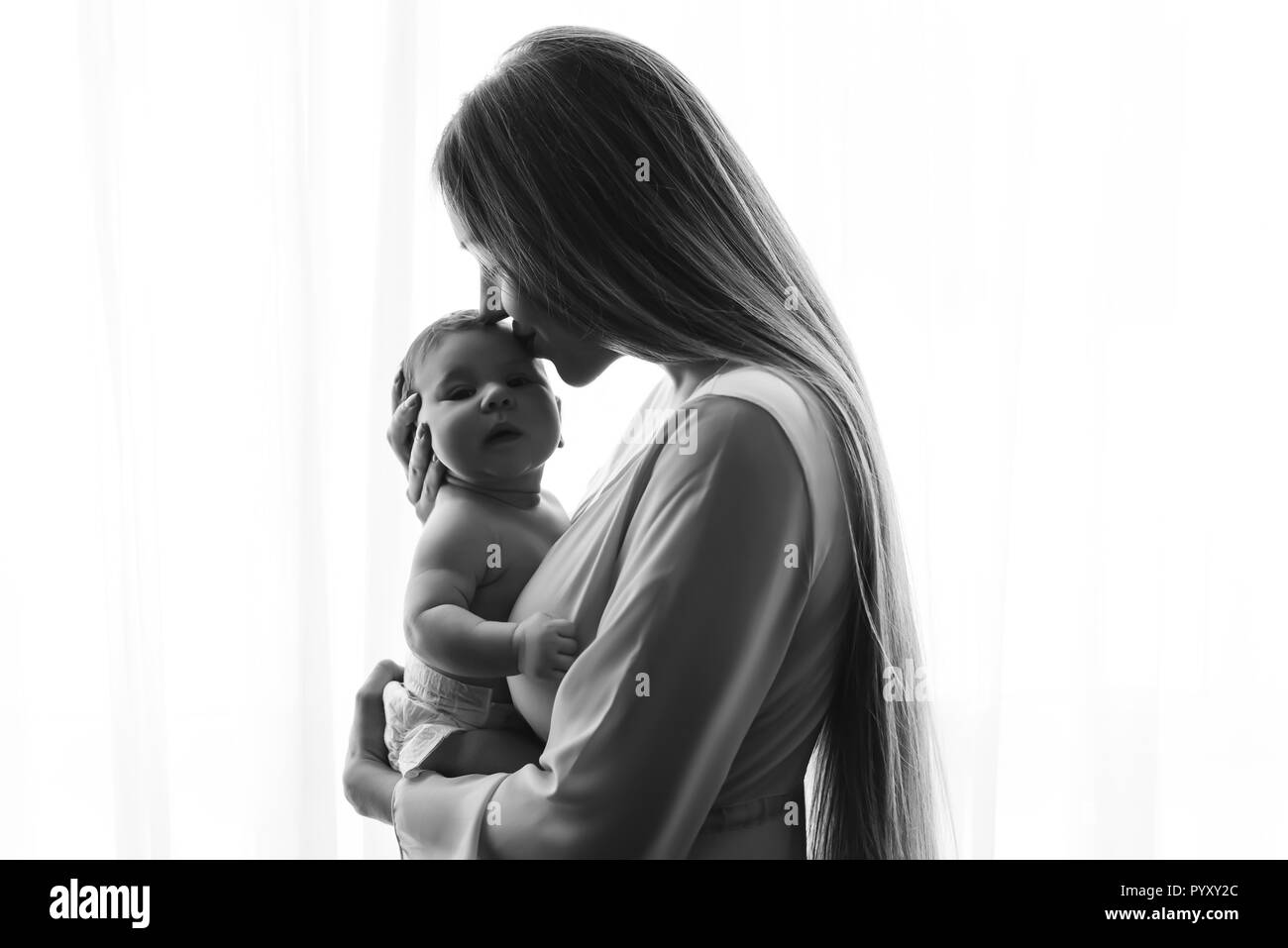 Schwarz-weiß Bild von Mutter küssen Baby Jungen vor der Vorhänge zu Hause Stockfoto