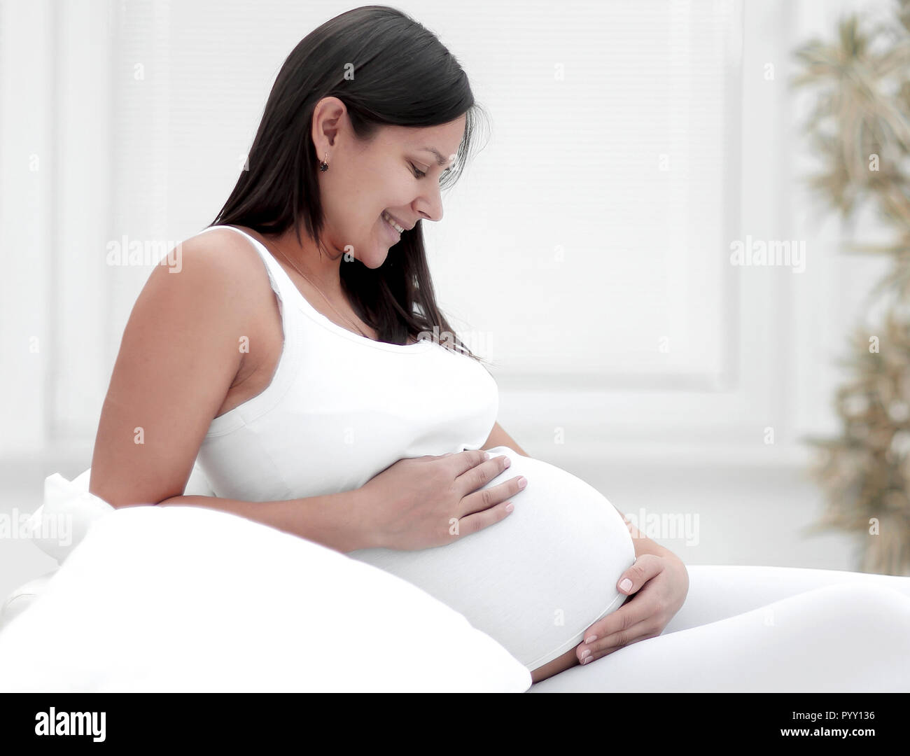 Schöne schwangere Frau am Sofa sitzen und halten Hand auf Bauch. Stockfoto