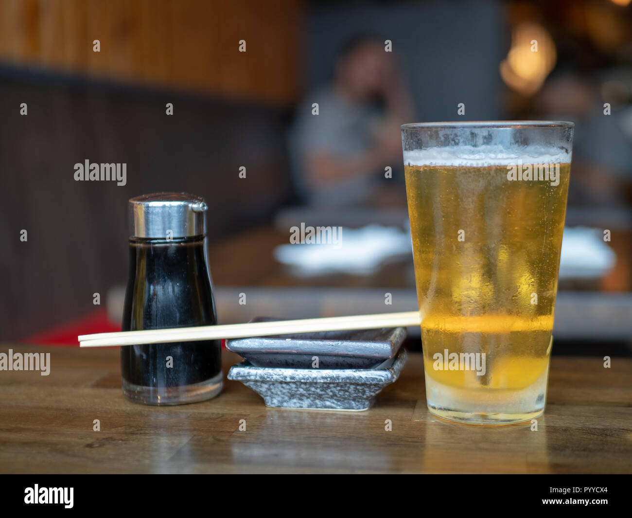 Sojasauce Dispenser, Gericht, Holz- Stäbchen, und Pint Glas mit Bier auf Tabelle ausgefüllt Stockfoto