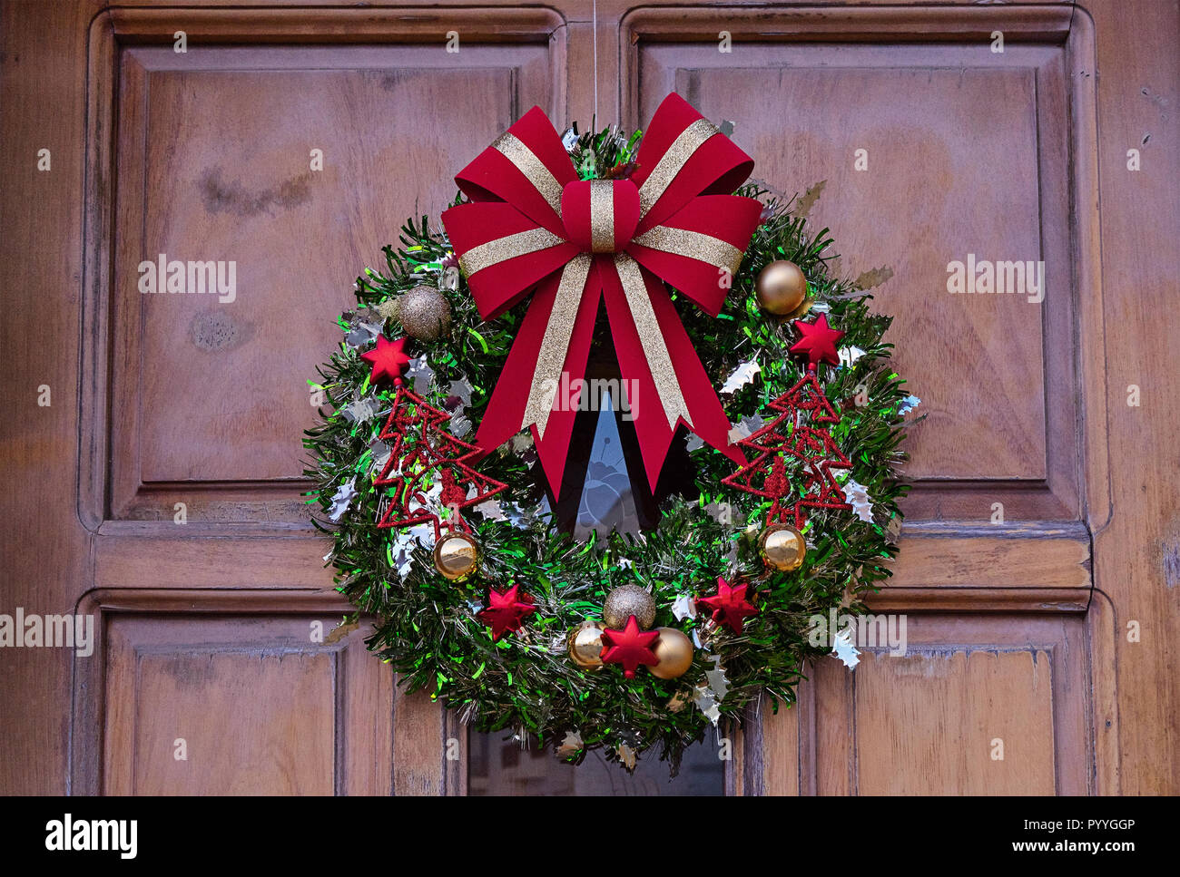 Traditionelle Weihnachtsbaum Kranz mit roter Schleife, Weihnachtskugeln und Glocken. Dekoration der vorderen Tür an der Schwelle zu Weihnachten Stockfotografie