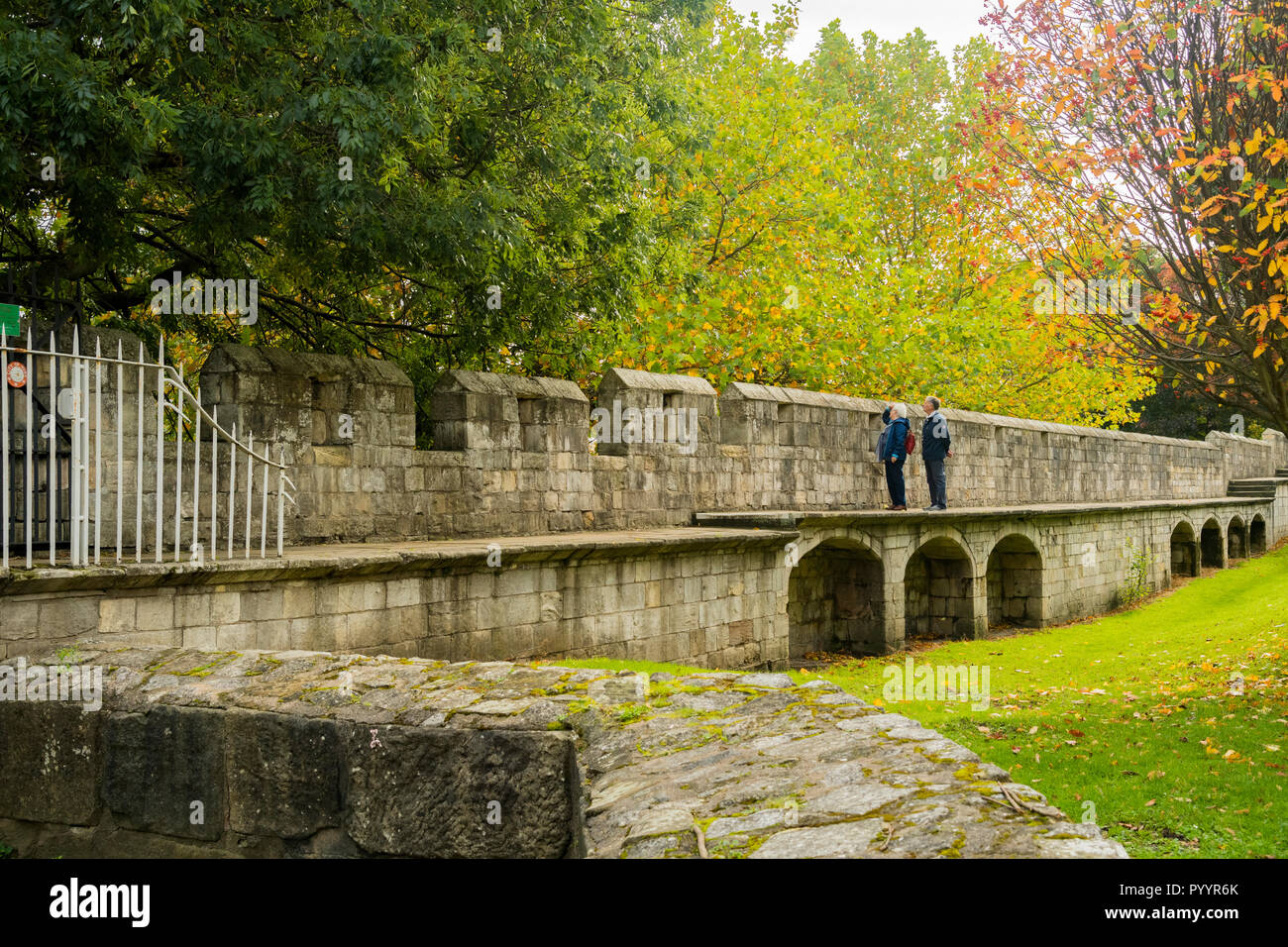 Herbsttag & Mann & Frau stehen zusammen und blicken vom Gehweg auf die wunderschöne historische mittelalterliche Stadtmauer von York - North Yorkshire, England, Großbritannien Stockfoto