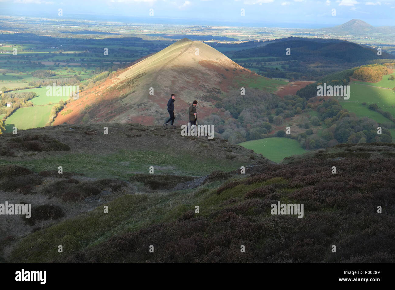 Zwei männliche Wanderer in der Nähe der Gipfel von Caer Caradoc, Church Stretton, Shropshire. Die Sonne leuchtet auf dem Höhepunkt der Lawley Hügel hinter Ihnen. In der weit entfernten Rechts ist die Wrekin Stockfoto