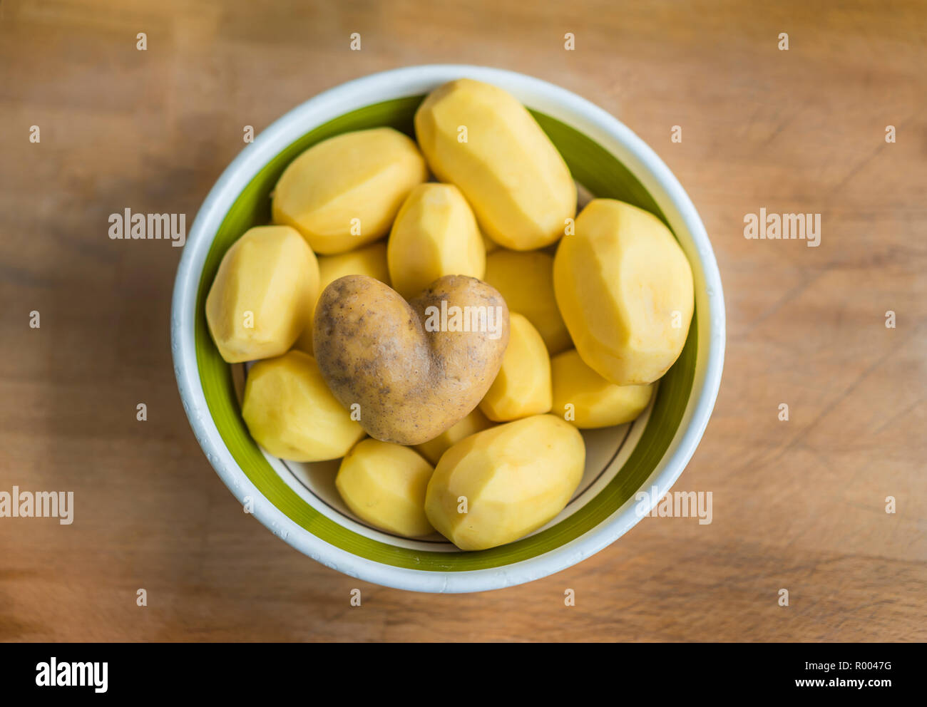 Schüssel von geschälten Kartoffeln, einer Herzförmigen ungeschälte Kartoffel auf der Oberseite Stockfoto