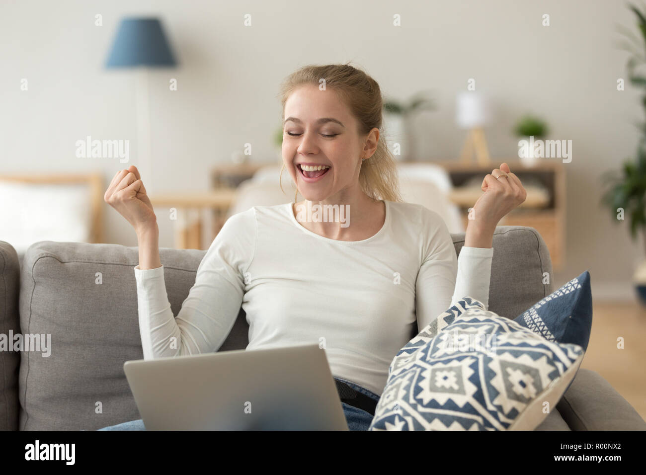 Fröhlich lachende Frau sitzt auf der Couch mit Laptop Stockfoto