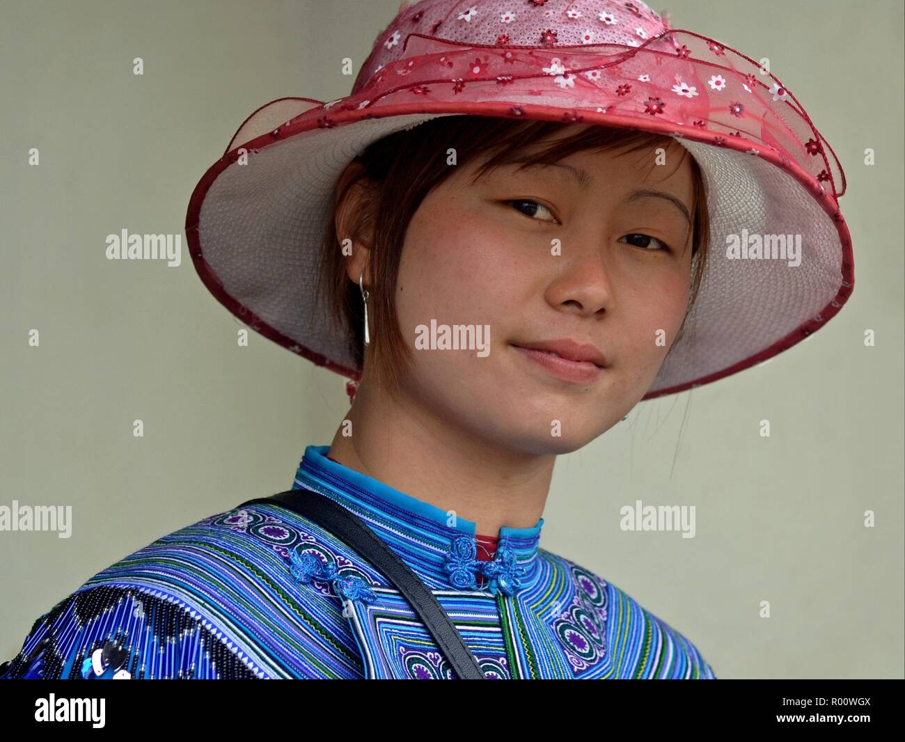 Junge vietnamesische H'Mong ethnische Minderheit Bergvolk Frau mit rosa Sonnenhut und bestickte traditionelle H'Mong Kleidung in Blau sieht in die Kamera. Stockfoto