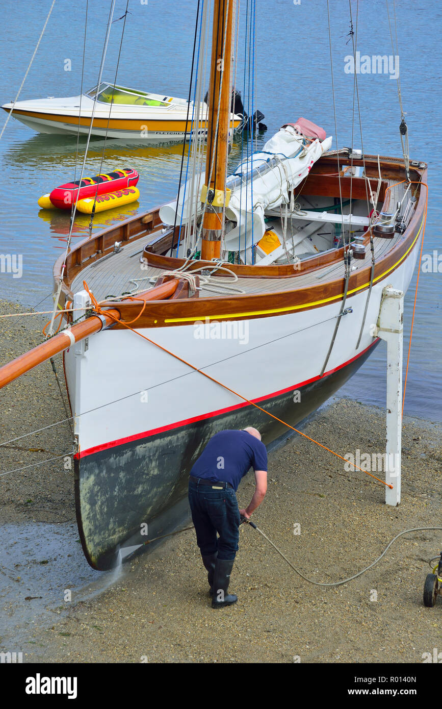 Macht Waschen der Rumpf eines Falmouth Arbeiten Boot am Strand von St Mawes, Roseland Halbinsel, Cornwall, South West England, Großbritannien Stockfoto