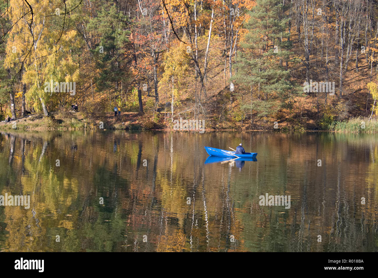 Schönen herbstlichen Wald spiegelt sich in den ruhigen Wassern des Sees, mit einem Fischer in einem blauen Boot Stockfoto