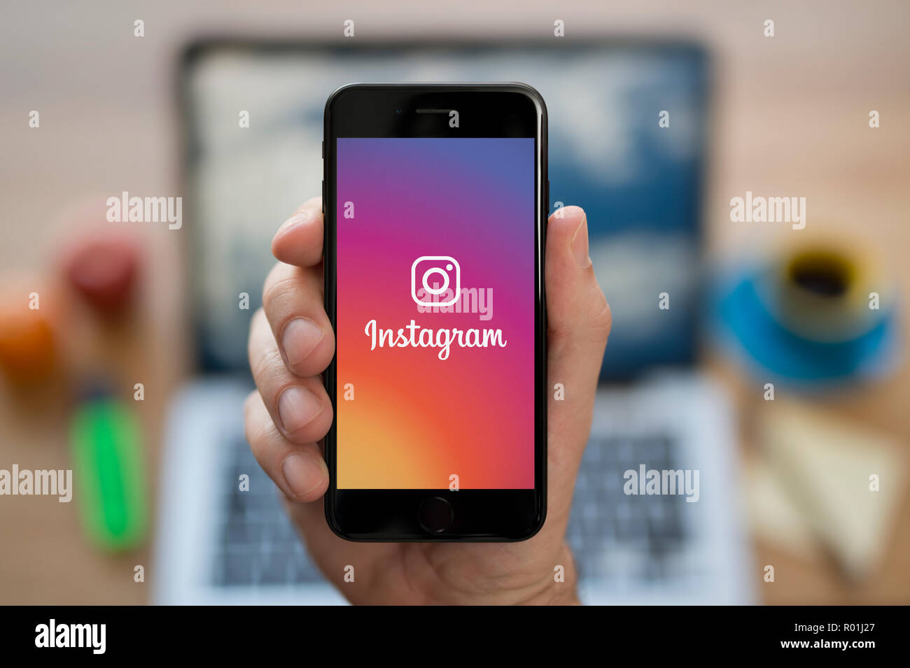 Ein Mann schaut auf seinem iPhone die zeigt die Instagram logo, während saß an seinem Computer Schreibtisch (nur redaktionelle Nutzung). Stockfoto