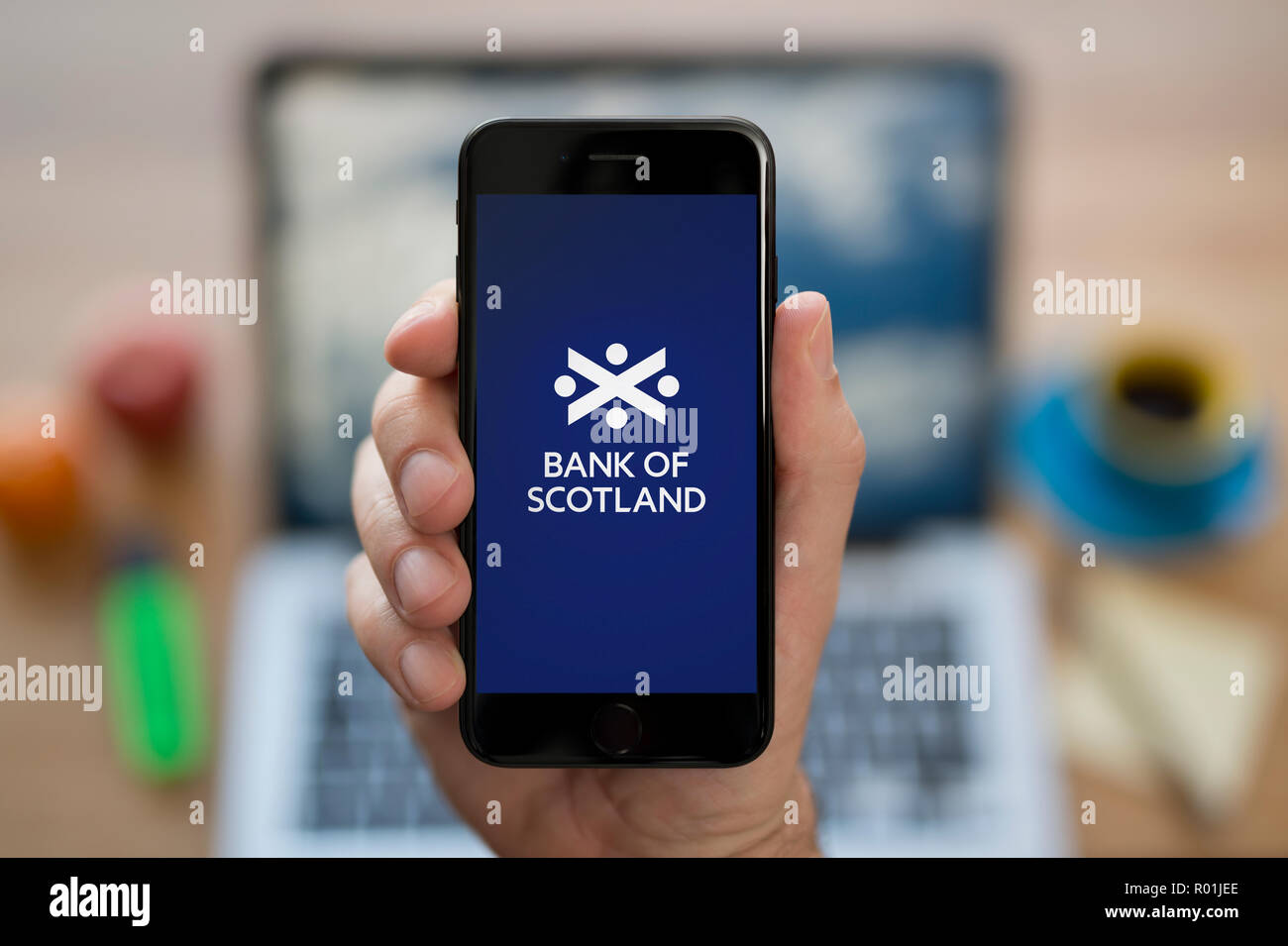 Ein Mann schaut auf seinem iPhone zeigt die Bank von Schottland logo, während saß an seinem Computer Schreibtisch (nur redaktionelle Nutzung). Stockfoto