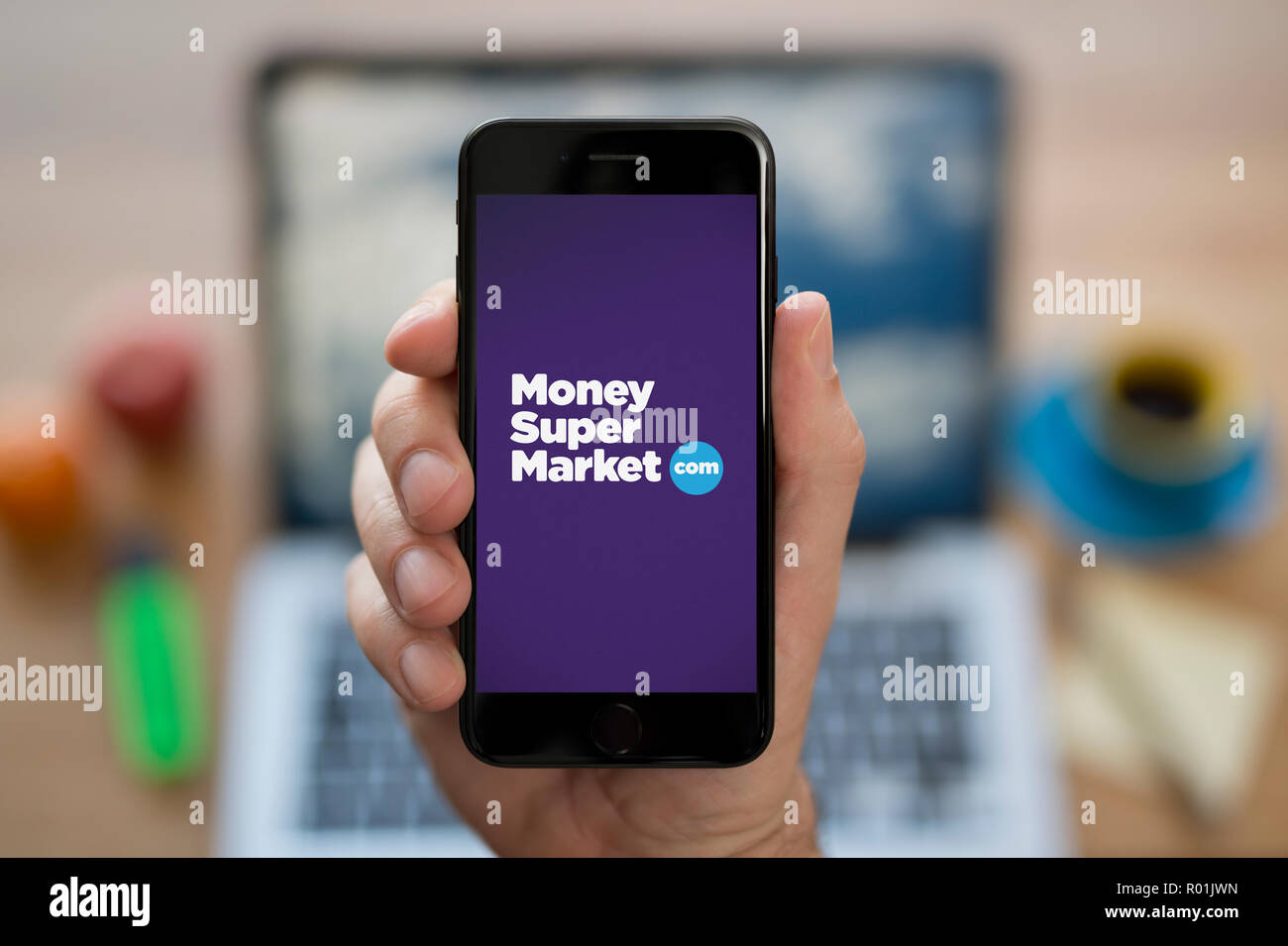 Ein Mann schaut auf seinem iPhone. Das Geld Supermarkt logo, während saß an seinem Computer Schreibtisch (nur redaktionelle Nutzung). Stockfoto