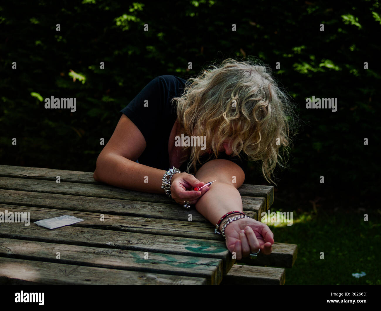 Eine Frau, die Injizierender Drogenkonsum in ihr Arm mit einer Spritze auf der Straße und eine Dosis der Droge zu der Seite Stockfoto