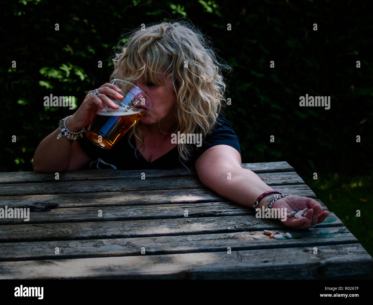 Eine Frau mit einer grossen Zahl von Tabletten in ihrer Hand in  verschiedenen Farben und Größen und ein Glas Bier, an einem Tisch im Freien  Stockfotografie - Alamy