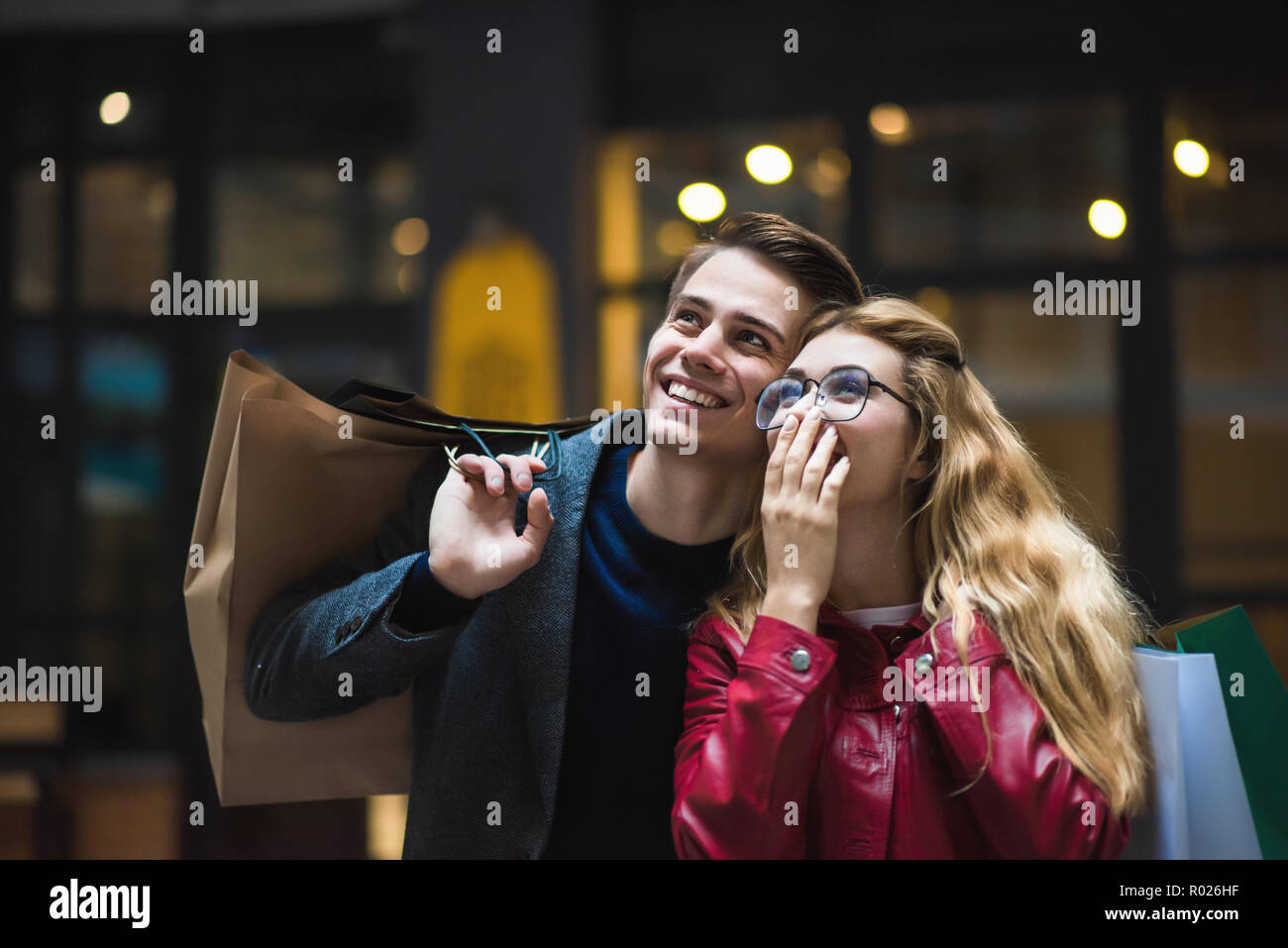 Schönes Paar mit Einkaufstüten spricht und lächelnd, während sie Shopping in der Mall konzentrieren sie sich auf die überraschten Frau. Stockfoto
