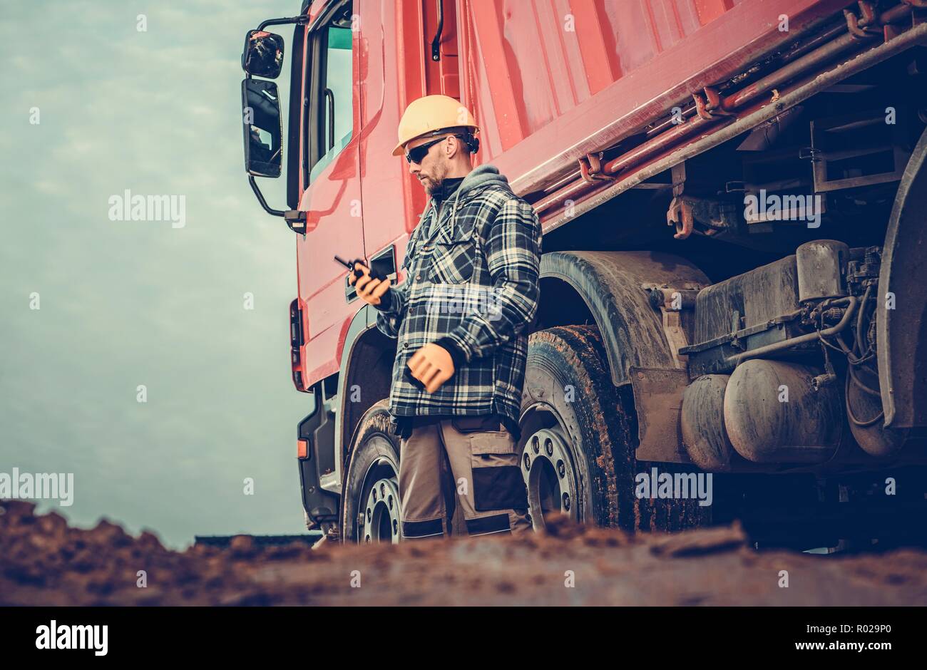 Kaukasische Dump Truck Fahrer in seinem 30s und die Baustelle voller Schmutz zu bewegen. Stockfoto