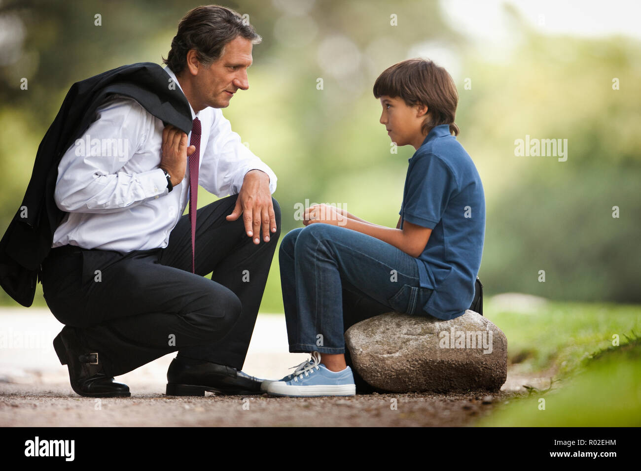 Corporate Mann zusammengekauert neben seinem Sohn auf dem Bürgersteig. Stockfoto