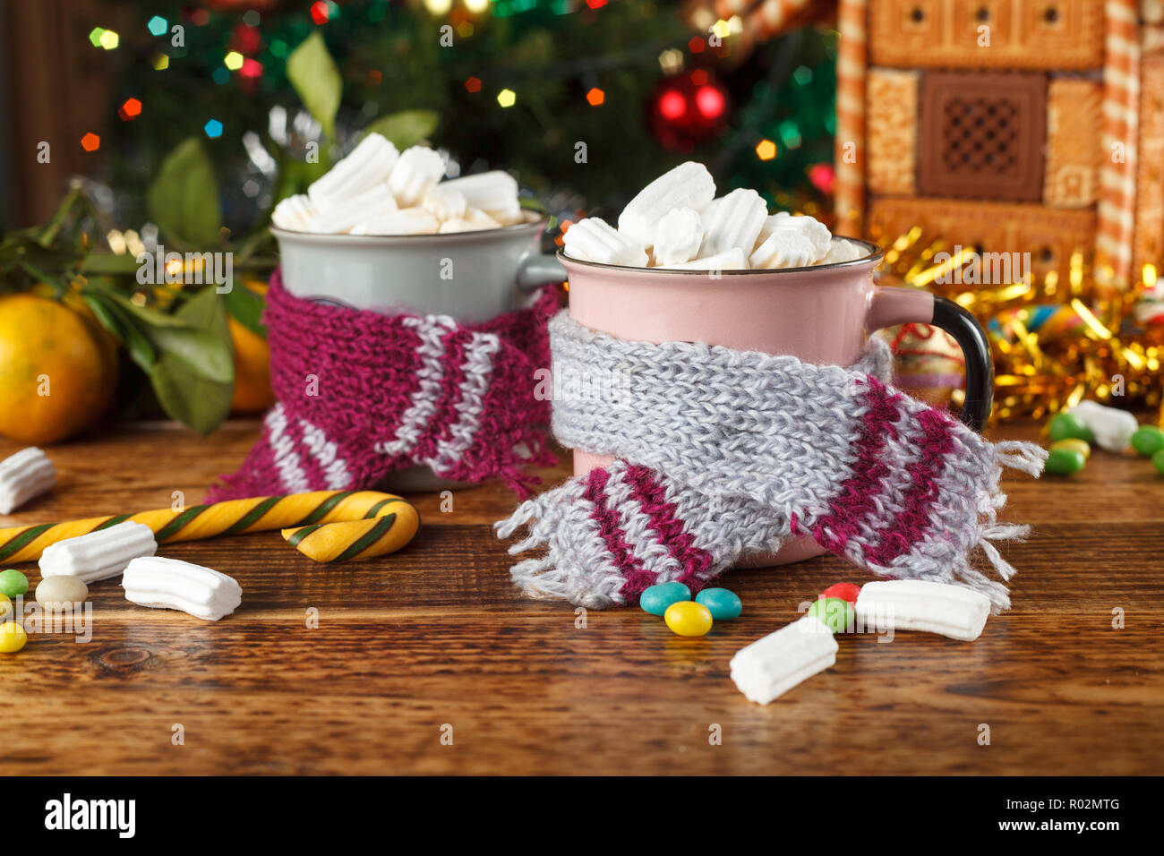 Zwei Tassen in Schals mit heißem süsses Getränk und Marshmallows auf dem Hintergrund einer Lebkuchenhaus. Close-up. Stockfoto